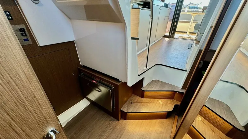 Slide: The Image of Lower Deck Access and Galley View This image showcases the elegant transition from the lower deck to the upper galley area of the 2022 Beneteau Antares 11. The warm wood tones of the staircase and cabinetry create a welcoming atmosphere, complemented by modern stainless steel appliances. - 7403683