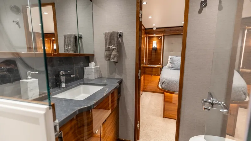 Slide: The Image of Luxurious Ensuite Bathroom and Stateroom This elegantly designed ensuite bathroom features a sleek countertop and modern fixtures, complemented by rich wood cabinetry. The doorway leads to a plush stateroom, showcasing a cozy bed with ambient lighting for a relaxing atmosphere. The sophisticated - 7531169