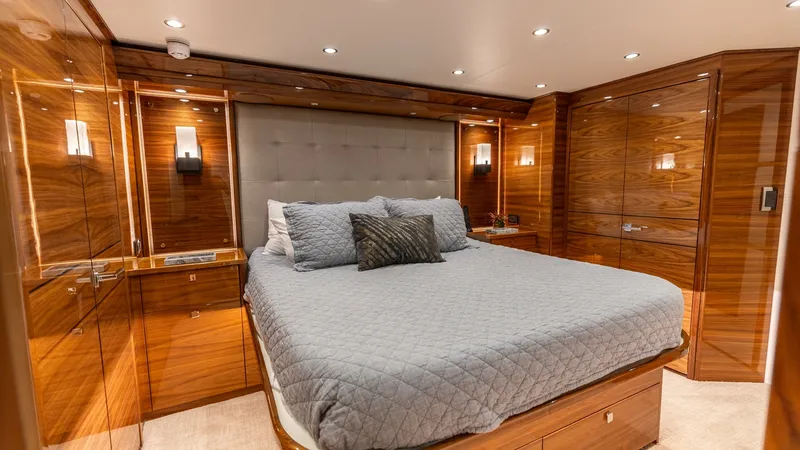Slide: The Image of Luxurious Master Stateroom Interior This elegant master stateroom on the 2025 Viking 74 Convertible features rich wooden paneling and a plush queen-sized bed. Ambient lighting and modern sconces provide a warm and inviting atmosphere, while ample storage is seamlessly integrated into the sl - 7531167