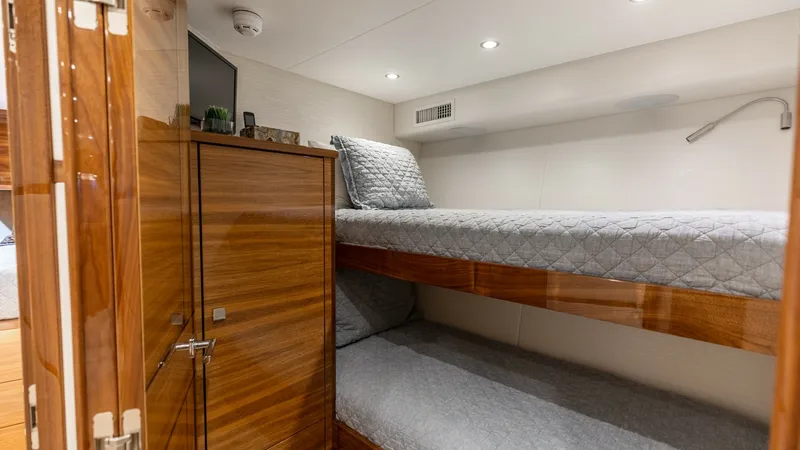 Slide: The Image of Guest Stateroom with Bunk Beds This cozy guest stateroom on the 2025 Viking 74 Convertible features comfortable bunk beds with plush bedding, perfect for accommodating additional guests. The room is elegantly appointed with rich wooden cabinetry providing ample storage space. Soft ambi - 7531179
