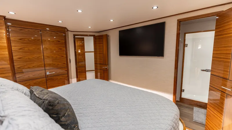 Slide: The Image of Master Stateroom with Ensuite Access The master stateroom of the 2025 Viking 74 Convertible offers a spacious and luxurious retreat. It features a plush, king-sized bed with elegant bedding, surrounded by rich wood cabinetry that provides ample storage. The room includes a large flat-screen - 7531168