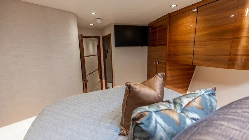 Slide: The Image of Guest Stateroom with TV and Storage This inviting guest stateroom features a plush bed adorned with luxurious pillows and a stylish blue quilt, offering a cozy retreat for guests. The room is equipped with a wall-mounted TV for entertainment and elegant high-gloss wooden cabinetry, providin - 7531172