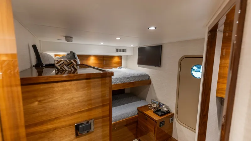 Slide: The Image of Cozy Bunk Stateroom This inviting bunk stateroom on the 2025 Viking 74 Convertible features rich wood finishes and plush bedding, creating a warm and comfortable retreat. Soft recessed lighting and a wall-mounted television enhance the space, while a porthole provides natura - 7531183