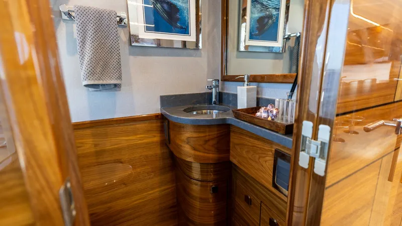Slide: The Image of Luxurious Guest Head Interior The guest head on the 2025 Viking 74 Convertible showcases exquisite craftsmanship with rich wood paneling and sleek fixtures. The elegantly curved vanity features a polished countertop and integrated sink, complemented by modern amenities. Nautical artwo - 7531164