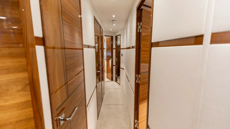 Slide: The Image of Elegant Interior Corridor This image showcases the sleek interior corridor of the 2025 Viking 74 Convertible, 'It Just Takes Time'. The hallway features high-gloss wooden doors and plush carpeting, creating a luxurious and inviting atmosphere. Recessed lighting enhances the warm t - 7531166