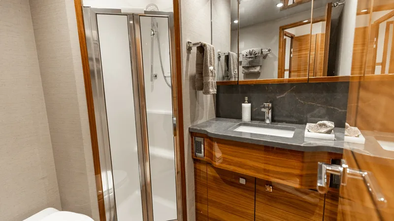 Slide: The Image of Elegant En-Suite Bathroom This en-suite bathroom on the 2025 Viking 74 Convertible exudes luxury with its sleek shower enclosure and high-gloss wooden cabinetry. The contemporary sink area features a polished countertop and ample storage, complemented by subtle ambient lighting. T - 7531173