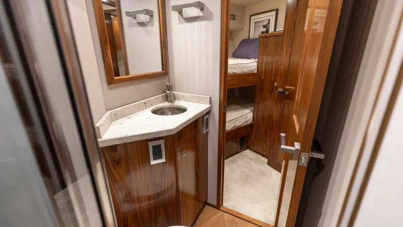 Slide: The Image of Guest Head and Bunk View This image features the guest head on the Viking 72 Convertible, showcasing elegant wood finishes and a sleek countertop with an integrated sink. The space is efficiently designed, maximizing utility and style, with a glimpse into a cozy bunk room. The lu - 7460592