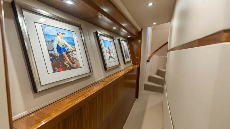 Slide: The Image of Elegant Lower Deck Hallway This image showcases the sophisticated lower deck hallway of the 2018 Viking 72 Convertible. The corridor features rich wooden paneling and artfully displayed framed prints, adding a touch of elegance. Soft overhead lighting highlights the plush carpeted - 7460582