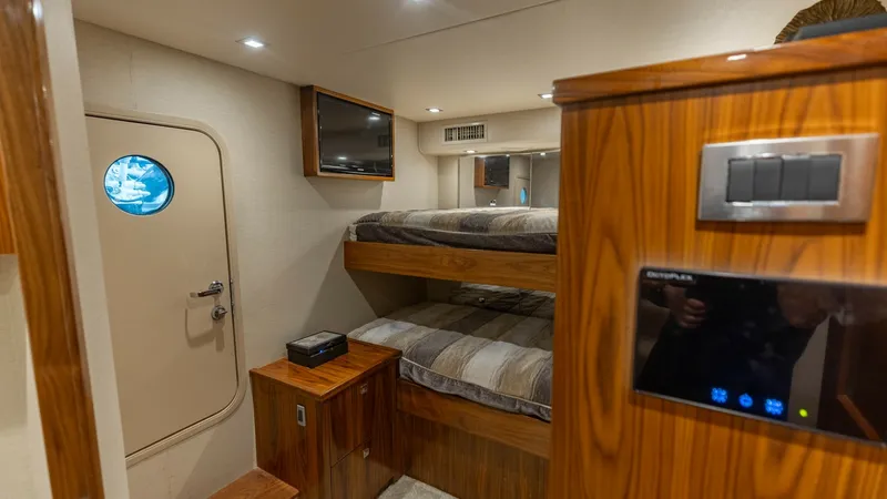 Slide: The Image of Guest Stateroom with Bunk Beds The guest stateroom on the Viking 72 Convertible offers cozy accommodations with stylish bunk beds and warm wood finishes. This intimate space features modern lighting, a small porthole for natural light, and a built-in entertainment system. The room's cl - 7460597