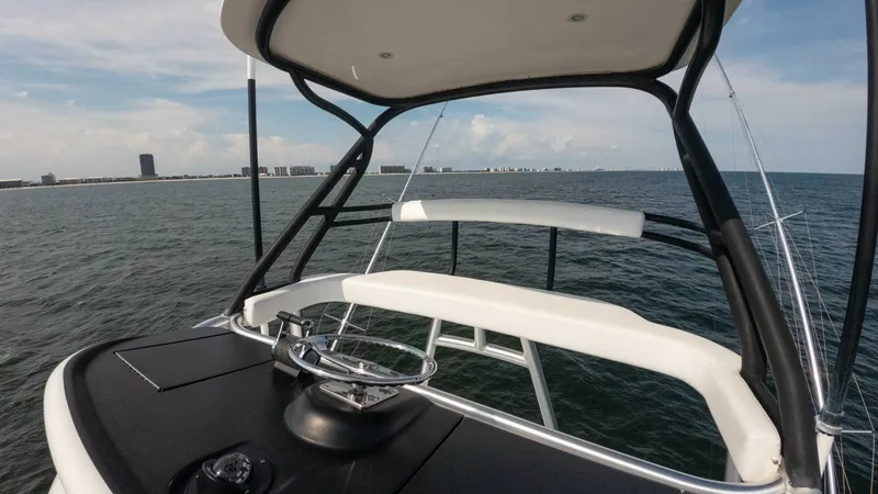 Slide: The Image of Flybridge Helm Station The flybridge helm station of the 2018 Viking 72 Convertible offers a commanding view over the water, featuring a sleek black dashboard and a stainless steel steering wheel. The white cushioned seating provides comfort, while the overhead bimini offers sh - 7460619