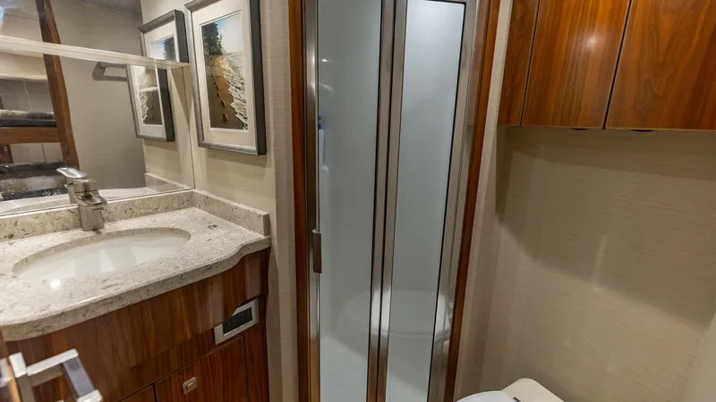 Slide: The Image of Luxury En-Suite Bathroom This elegant en-suite bathroom aboard the 2018 Viking 72 Convertible features a sleek vanity with a polished stone countertop and modern sink. The enclosed shower boasts frosted glass doors, offering both style and privacy. Rich wood cabinetry and tastefu - 7460595