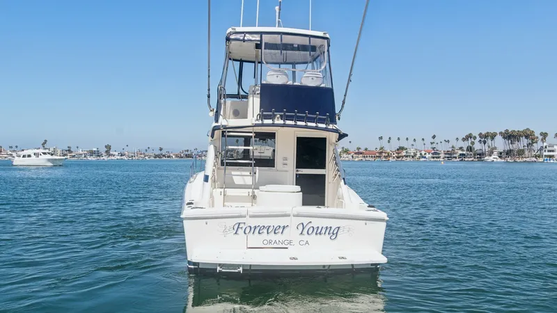 Slide: The Image of Aft View with Flybridge The aft view of the 1998 Riviera Convertible 'Forever Young' showcases its spacious cockpit and inviting flybridge. The flybridge provides excellent visibility and is equipped with comfortable seating, perfect for navigating or relaxing. The vessel's name - 7415865