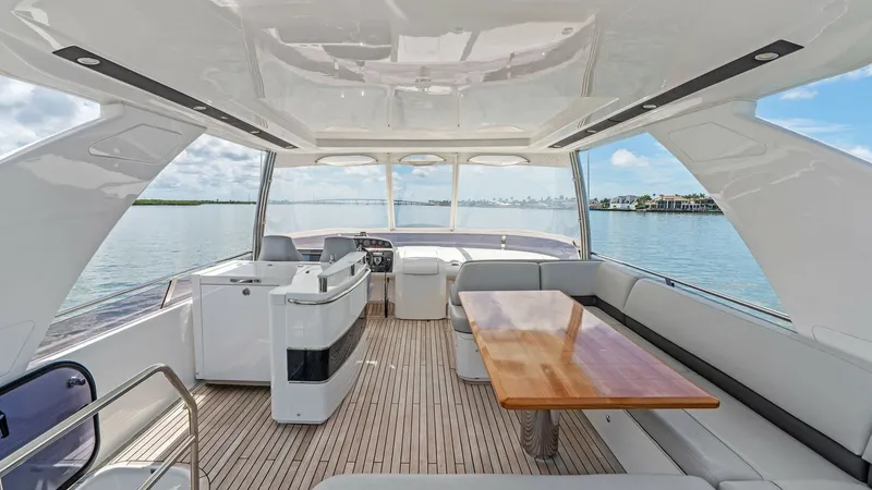 Slide: The Image of Spacious Flybridge with Seating Area The flybridge of the 2016 Princess 64, 'No Vacansea', offers a luxurious open-air retreat with panoramic views. Featuring ample seating with plush cushions and a sleek wooden dining table, this area is ideal for entertaining. The helm station provides exc - 7460849