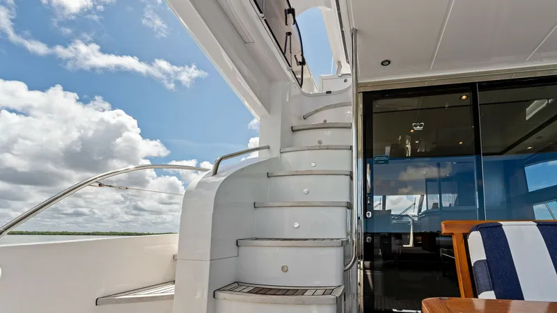 Slide: The Image of Flybridge Staircase and Aft Deck This image showcases the elegant staircase leading to the flybridge of the 2016 Princess 64 Flybridge yacht, No Vacansea. The sleek, curved steps are finished with teak accents, providing both style and safety. Adjacent to the staircase, the aft deck offe - 7460848