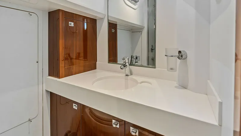 Slide: The Image of Crew Bathroom Vanity This sophisticated bathroom vanity features a sleek white countertop paired with rich wooden cabinetry, offering ample storage space. The modern faucet and integrated sink provide a clean and seamless look, while the mirrored wall enhances the sense of sp - 7460875