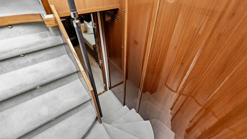 Slide: The Image of Staircase to Lower Deck Cabins This image showcases the elegant staircase leading to the lower deck cabins of the 2016 Princess 64 Flybridge. The steps are carpeted in a soft grey, complementing the high-gloss wooden paneling that adds a touch of luxury. The design ensures easy access - 7460821