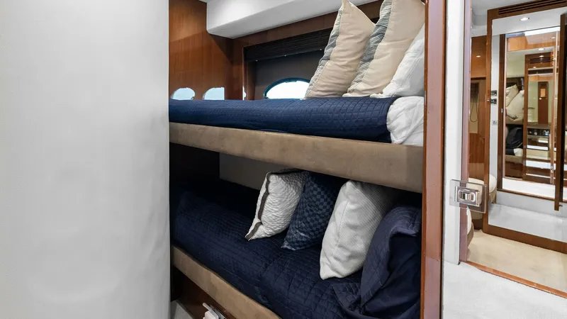 Slide: The Image of Cozy Twin Bunk Cabin This inviting twin bunk cabin on the Princess 64 Flybridge features a sleek and modern design with rich wood finishes. The comfortable bunks are dressed in stylish navy bedding, complemented by ample pillows for added comfort. A large window allows natura - 7460846