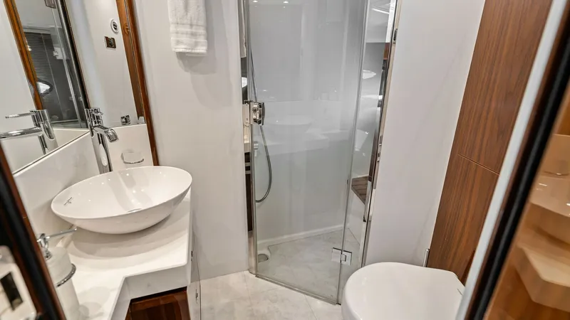 Slide: The Image of Elegant Onboard Bathroom with Shower This luxurious bathroom on the Princess 64 Flybridge features a stylish vessel sink atop a sleek countertop, complemented by rich wood cabinetry. A glass-enclosed shower offers a modern touch, enhancing the space's elegant design. The combination of white - 7460839