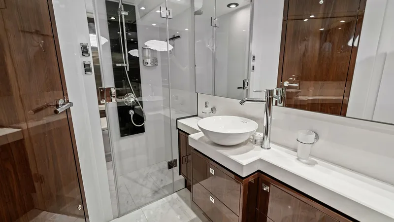 Slide: The Image of Luxurious Yacht Master Bathroom This elegant bathroom on the Princess 64 Flybridge features high-gloss wooden cabinetry and a sleek, contemporary design. The spacious layout includes a modern vessel sink atop a pristine countertop, complemented by ample storage. A glass-enclosed shower - 7460830