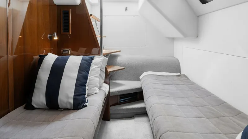Slide: The Image of Twin Crew Cabin Interior View This cozy twin guest cabin on the Princess 64 Flybridge features two comfortable single berths with plush grey bedding. The space is accented by warm wood paneling and a striped accent pillow, adding a touch of nautical elegance. Ample natural light filte - 7460873