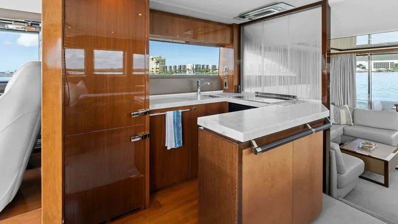 Slide: The Image of Galley and Salon Area The galley of the Princess 64 Flybridge showcases elegant high-gloss cabinetry and sleek countertops, providing a modern and functional cooking space. Large windows flood the area with natural light, offering stunning views of the surroundings. Adjacent t - 7460818