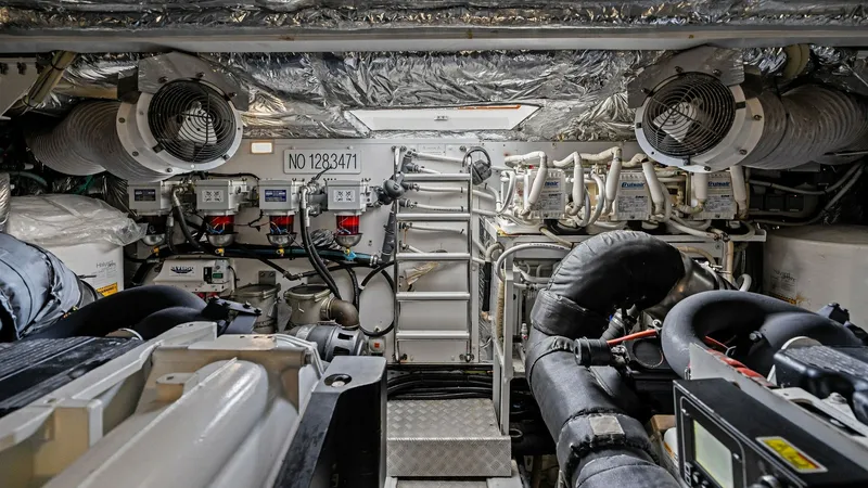 Slide: The Image of Engine Room with Twin CAT C18 ACERT Engines The engine room of the 2016 Princess 64 Flybridge 'No Vacansea' showcases a meticulously organized space featuring twin engines. The area is lined with reflective insulation, enhancing both temperature control and efficiency. Advanced systems and controls - 7460881
