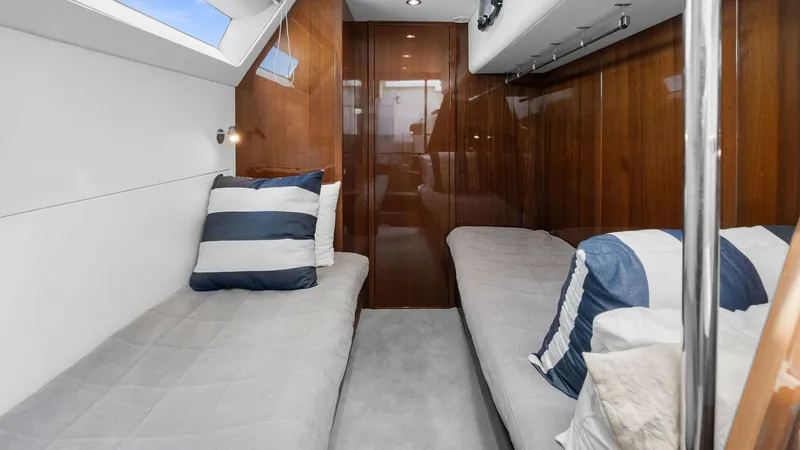 Slide: The Image of Twin Crew Cabin This inviting twin guest cabin features sleek wood paneling and plush bedding for a comfortable stay. The room is illuminated by natural light from the overhead window, creating a bright and airy atmosphere. Thoughtful details, such as striped throw pillo - 7460872