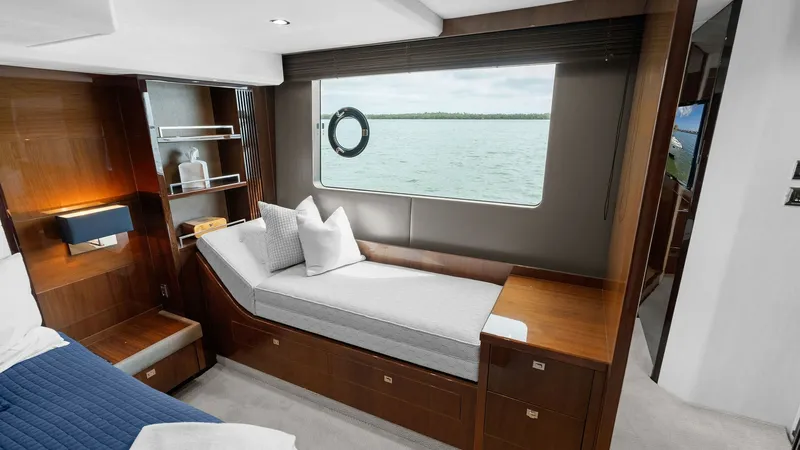 Slide: The Image of Luxurious Master Stateroom with Ocean View This elegant guest stateroom on the 2016 Princess 64 Flybridge features a cozy daybed with plush cushions, perfect for relaxation while enjoying panoramic sea views through the large window. The warm wood finishes and soft lighting create an inviting atmo - 7460823