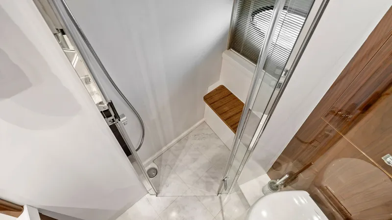 Slide: The Image of Elegant Yacht Bathroom with Shower This luxurious bathroom aboard the 2016 Princess 64 Flybridge features a sleek, glass-enclosed shower with a modern chrome fixture. The space is enhanced by elegant marble flooring and a wooden bench, providing both style and functionality. A large portho - 7460841