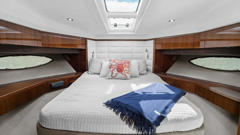 Slide: The Image of Luxurious Forward Stateroom View This elegant forward stateroom on the 2016 Princess 64 Flybridge offers a spacious and inviting retreat. The room features a plush double bed with stylish bedding, complemented by rich wood finishes and ample natural light from the overhead skylight. Buil - 7460834
