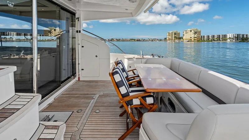 Slide: The Image of Spacious Aft Deck with Seating Area The aft deck of the 2016 Princess 64 Flybridge 'No Vacansea' offers an inviting outdoor space with elegant teak flooring and comfortable seating. A polished wooden dining table is surrounded by plush chairs and a cushioned bench, perfect for alfresco dini - 7460805