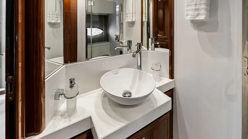 Slide: The Image of Elegant Ensuite Bathroom Vanity This luxurious ensuite bathroom on the 2016 Princess 64 Flybridge features a sleek, modern vanity with a stylish vessel sink. The high-gloss wood cabinetry adds warmth and sophistication, while ample mirrored surfaces enhance the sense of space and light. - 7460837