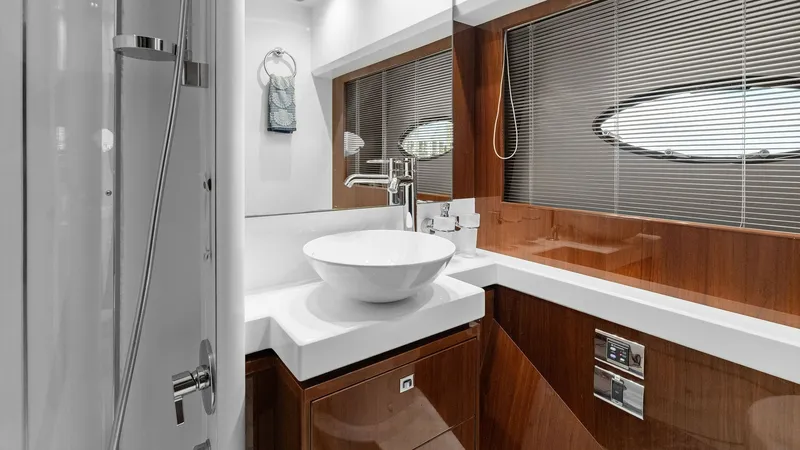 Slide: The Image of Luxurious Ensuite Bathroom This elegant ensuite bathroom on the 2016 Princess 64 Flybridge features a sleek vessel sink atop a glossy wood-finished vanity. The space is accentuated by modern fixtures, ample lighting, and a stylish porthole window, offering both functionality and so - 7460838