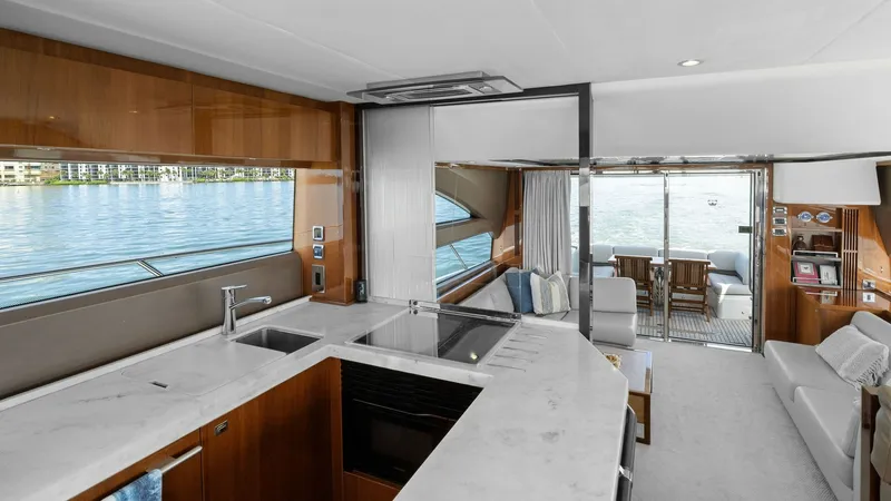 Slide: The Image of Galley and Salon with Aft View The galley of the 2016 Princess 64 Flybridge features sleek countertops and modern appliances, seamlessly integrating into the open-plan salon. Large windows flood the space with natural light, offering panoramic views of the water. The aft deck is visibl - 7460819