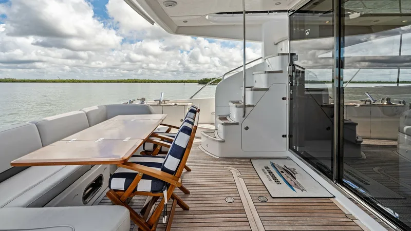 Slide: The Image of Aft Deck with Dining Area This luxurious aft deck on the 2016 Princess 64 Flybridge features a spacious dining area with elegant wooden chairs and a sleek table, perfect for alfresco meals. The rich teak flooring complements the sophisticated design, while the glass doors provide - 7460806