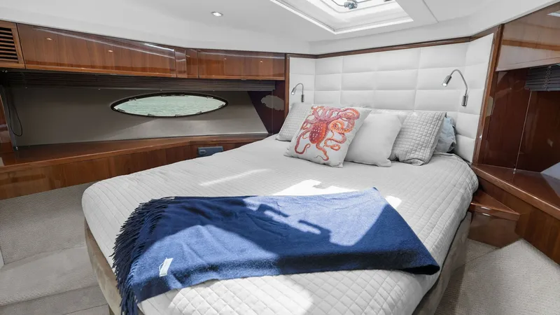 Slide: The Image of Forward Stateroom with Skylight The forward stateroom of the 2016 Princess 64 Flybridge offers a luxurious retreat with its plush double bed and elegant wood finishes. Natural light floods the space through a large skylight and side porthole, enhancing the room's airy ambiance. The soft - 7460835
