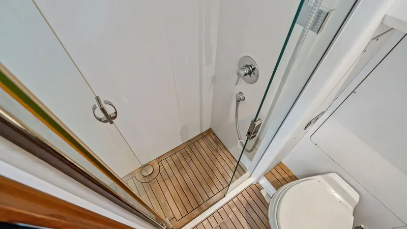 Slide: The Image of Crew Bathroom with Shower This well-designed bathroom on the Princess 64 Flybridge features a sleek, glass-enclosed shower and elegant wood flooring. The compact layout maximizes space, offering convenience and functionality. Modern fixtures and clean lines contribute to a luxurio - 7460876