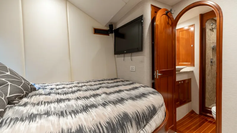 Slide: The Image of Cozy Guest Stateroom with Ensuite This inviting guest stateroom aboard the 2006 Blackwell 65 Convertible features a plush double bed with stylish bedding and a wall-mounted TV for entertainment. The warm wood tones of the arched door lead to a private ensuite bathroom, complete with polis - 7469756