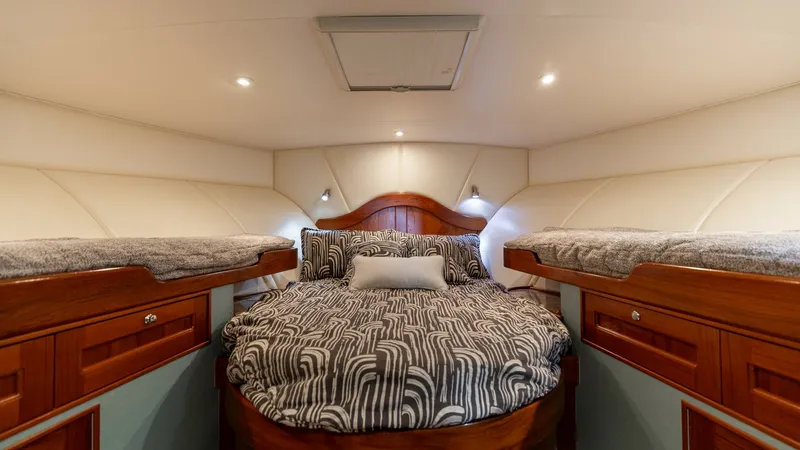 Slide: The Image of Forward Stateroom with Twin Berths The forward stateroom of the 2006 Blackwell 65 Convertible boasts a luxurious arrangement with a central double berth flanked by twin upper bunks. Rich wood cabinetry and elegant upholstery enhance the cozy ambiance, while recessed lighting creates a warm - 7469761
