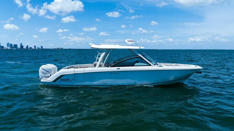 The Image of Side Profile on 320 Vantage The 2019 Boston Whaler 320 Vantage, 'Thou Shell Knot', glides effortlessly across the water, showcasing its sleek and modern design. The vessel's robust hull and spacious deck are highlighted against the backdrop of a clear blue sky and distant city skyli - 7469806
