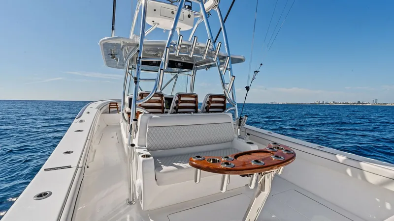 Slide: The Image of Center Console and Helm Seating The Valhalla V-41's center console area showcases premium helm seating with plush, diamond-stitched upholstery. The polished stainless steel T-top provides shade and houses additional rod holders for convenience. A robust teak fighting chair is prominentl - 7517258