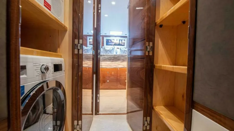 Slide: The Image of Laundry Area and Storage Space The image showcases a compact yet functional laundry area aboard the 2023 Viking 64 Convertible, featuring a modern washer and dryer set. Adjacent to the appliances is ample shelving for storage, crafted from quality wood, adding both utility and elegance - 7600536