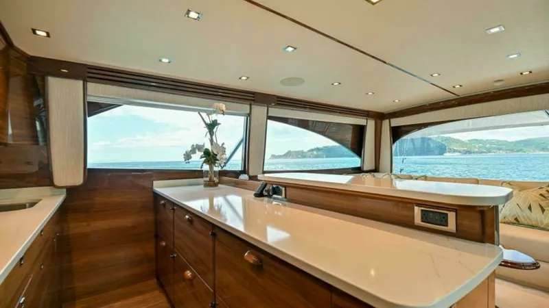 Slide: The Image of Galley and Salon with Ocean Views This elegant galley in the 2023 Viking 64 Convertible features sleek, polished wood cabinetry and expansive countertops, offering ample space for culinary preparation. Large windows flood the area with natural light and provide stunning panoramic views of - 7600517