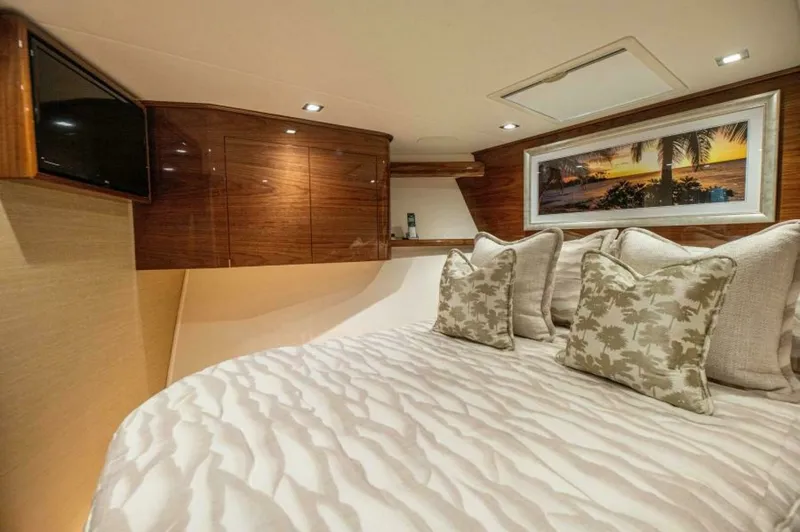 Slide: The Image of Luxurious Forward Stateroom The forward stateroom of the 2023 Viking 64 Convertible boasts elegant wood finishes and plush bedding, creating a warm and inviting atmosphere. The room features recessed lighting and a mounted television for entertainment, complemented by tasteful artwo - 7530856