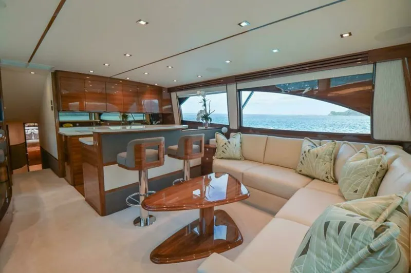 Slide: The Image of Spacious Salon with Galley View This luxurious salon aboard the 2023 Viking 64 Convertible features a plush L-shaped sofa complemented by a sleek, high-gloss wooden coffee table. The open galley is equipped with modern bar stools and high-end finishes, perfect for entertaining. Large wi - 7530828