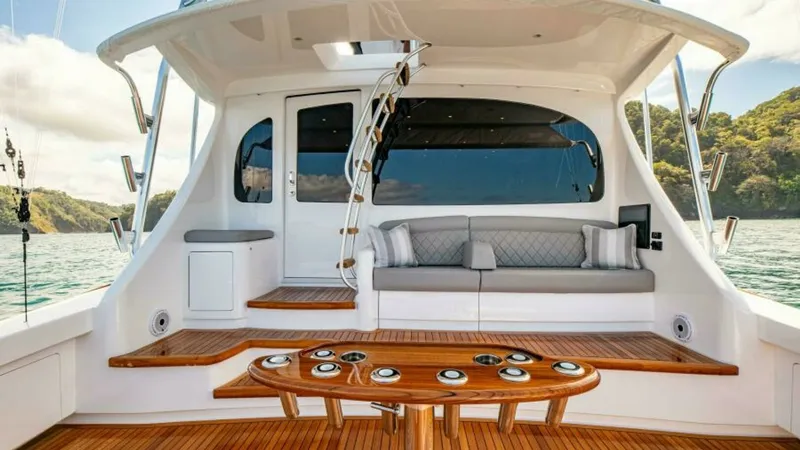 Slide: The Image of Aft Deck with Seating and Table The aft deck of the 2023 Viking 64 Convertible features elegant teak flooring and a spacious seating area with plush cushions, perfect for relaxation or entertaining. The central table is ideal for casual dining, while the unobstructed view of the water e - 7600541