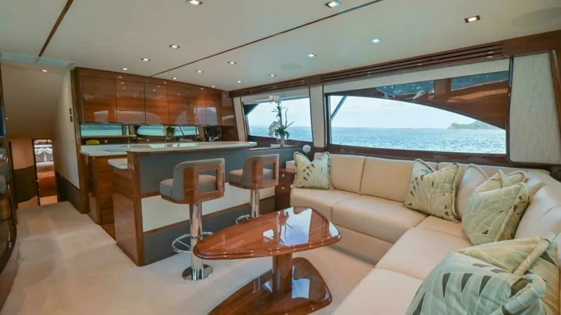 Slide: The Image of Spacious Salon with Galley View This luxurious salon aboard the 2023 Viking 64 Convertible features a plush L-shaped sofa complemented by a sleek, high-gloss wooden coffee table. The open galley is equipped with modern bar stools and high-end finishes, perfect for entertaining. Large wi - 7600510