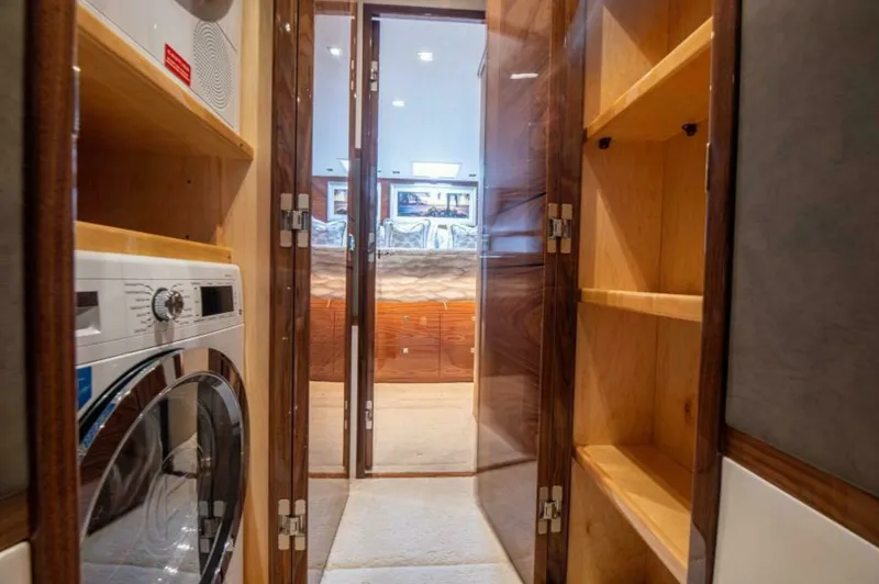 Slide: The Image of Laundry Area and Storage Space The image showcases a compact yet functional laundry area aboard the 2023 Viking 64 Convertible, featuring a modern washer and dryer set. Adjacent to the appliances is ample shelving for storage, crafted from quality wood, adding both utility and elegance - 7530854