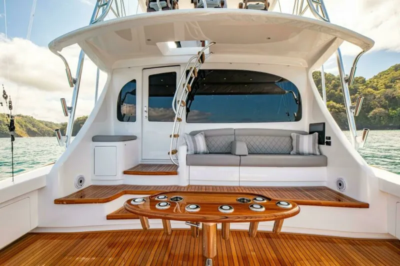 Slide: The Image of Aft Deck with Seating and Table The aft deck of the 2023 Viking 64 Convertible features elegant teak flooring and a spacious seating area with plush cushions, perfect for relaxation or entertaining. The central table is ideal for casual dining, while the unobstructed view of the water e - 7530859