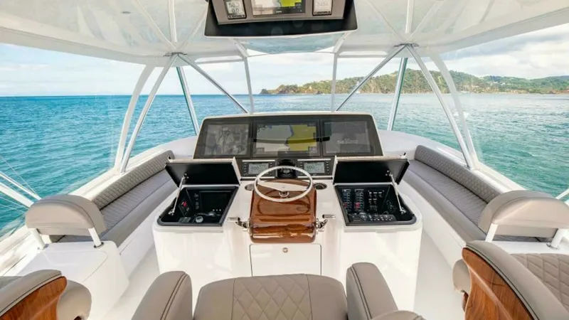 Slide: The Image of Flybridge Helm Station The helm station on the flybridge of the 2023 Viking 64 Convertible offers a commanding view of the surrounding waters. It features a state-of-the-art navigation system with multiple displays and ergonomic controls. The luxurious, quilted seating and teak - 7600543